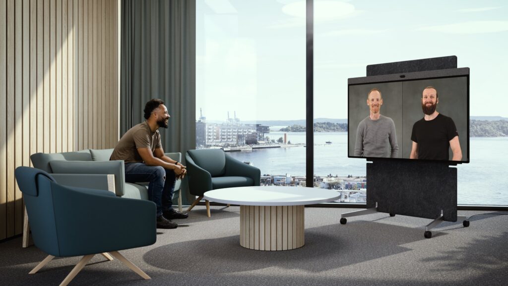 A mobile meeting board on a rolling stand in an open lounge space, showing two remote participants during a hybrid meeting